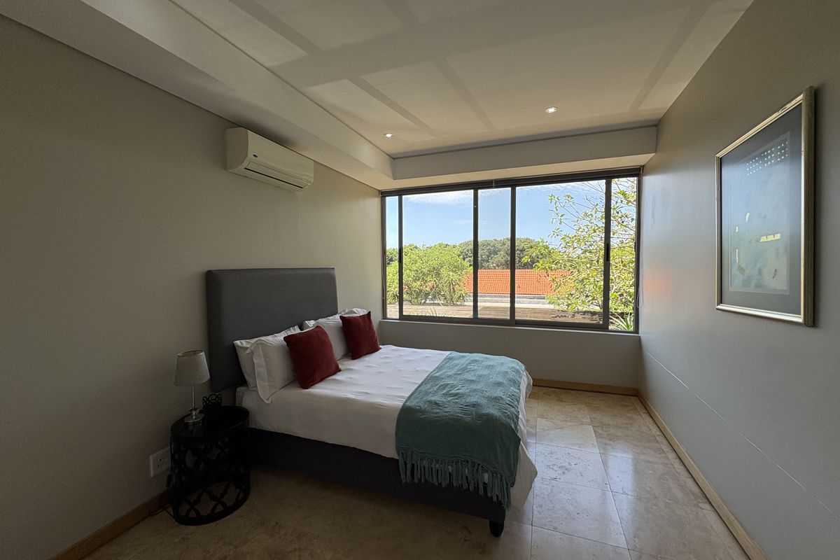 A well-lit bedroom featuring large windows, tiled flooring, and a wall-mounted air conditioning unit.