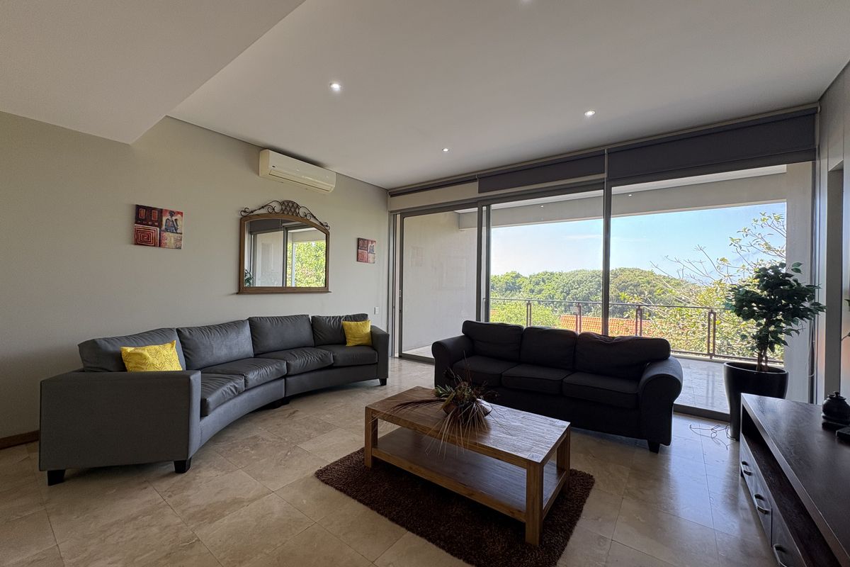 Spacious living room featuring large sliding glass doors that open onto a covered balcony with scenic views, complemented by recessed lighting and tiled flooring.
