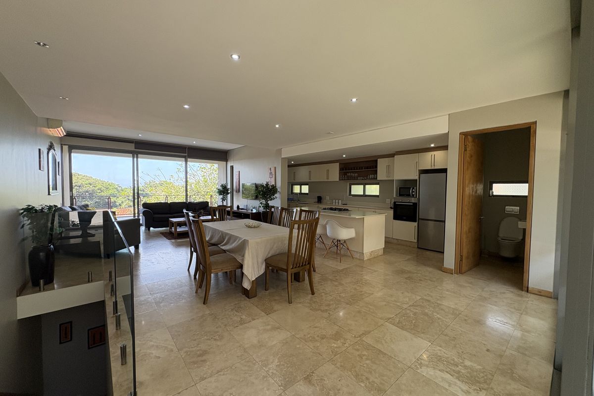 Open-plan living area featuring a modern kitchen with built-in cabinetry, dining space, and lounge area with large sliding doors leading to an outdoor view.