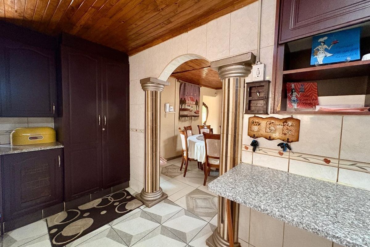 A kitchen area featuring dark cabinetry, granite-look countertops, and a distinctive arched entryway with decorative columns leading into the dining space.