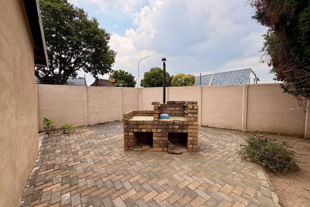 A private rear courtyard featuring a built-in brick braai and paved flooring, enclosed by high boundary walls for added privacy.