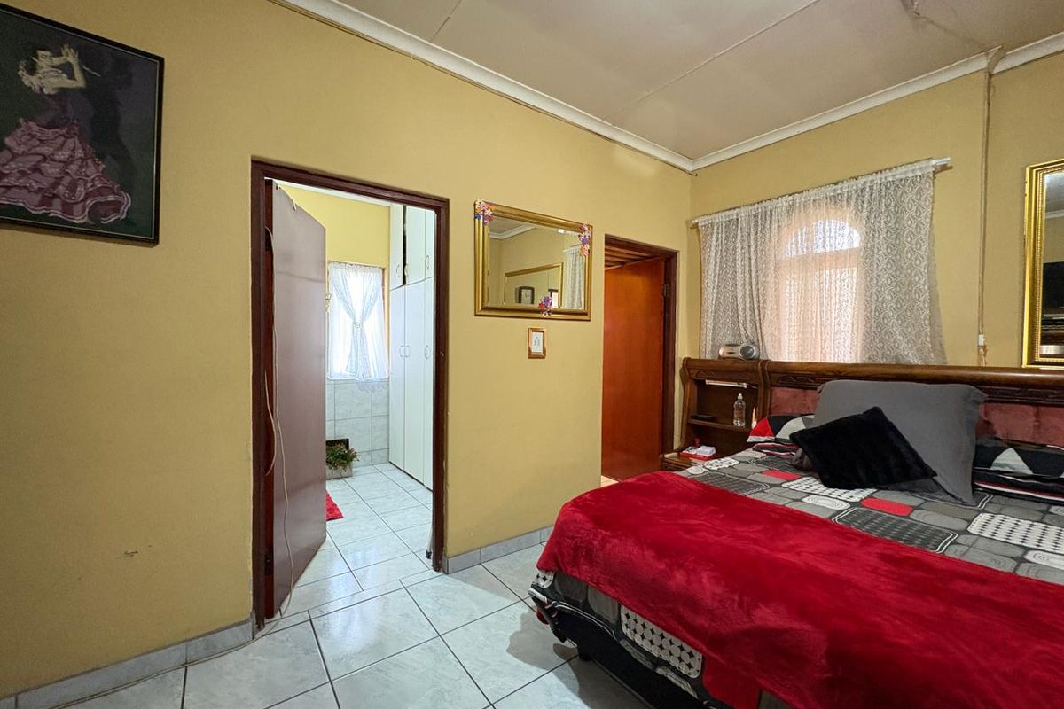 A bedroom featuring tiled flooring and an adjoining dressing area with built-in cupboards, providing functional living space.