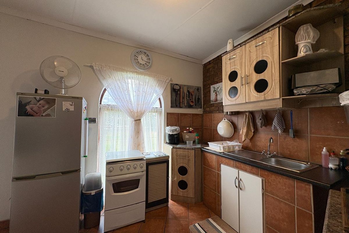 A functional kitchen featuring tiled flooring, brick accent wall, built-in cabinetry, and a freestanding stove, illuminated by a large arched window.