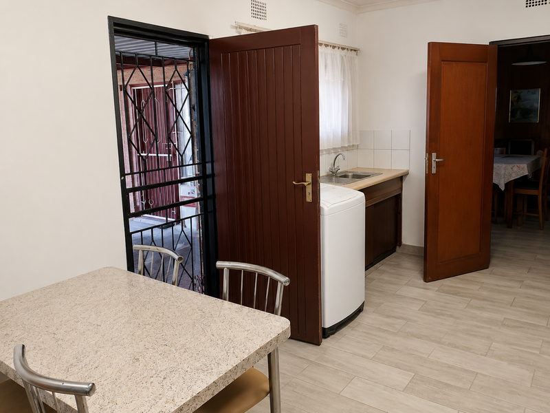 A functional laundry area featuring a stainless steel sink, tiled splashback, and timber cabinetry, with direct access to an outdoor security gate.