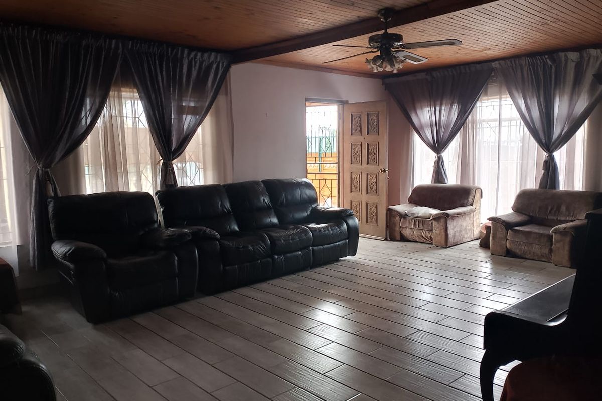 Spacious living room featuring a timber-clad ceiling, ceiling fan, and tiled flooring, providing a comfortable and functional living space.