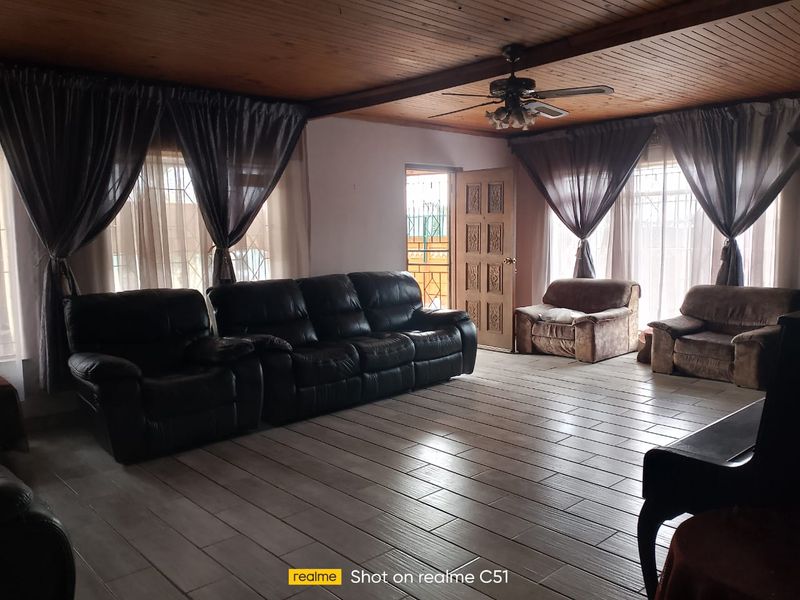 Spacious living room featuring a timber-clad ceiling, ceiling fan, and tiled flooring, providing a comfortable and functional living space.