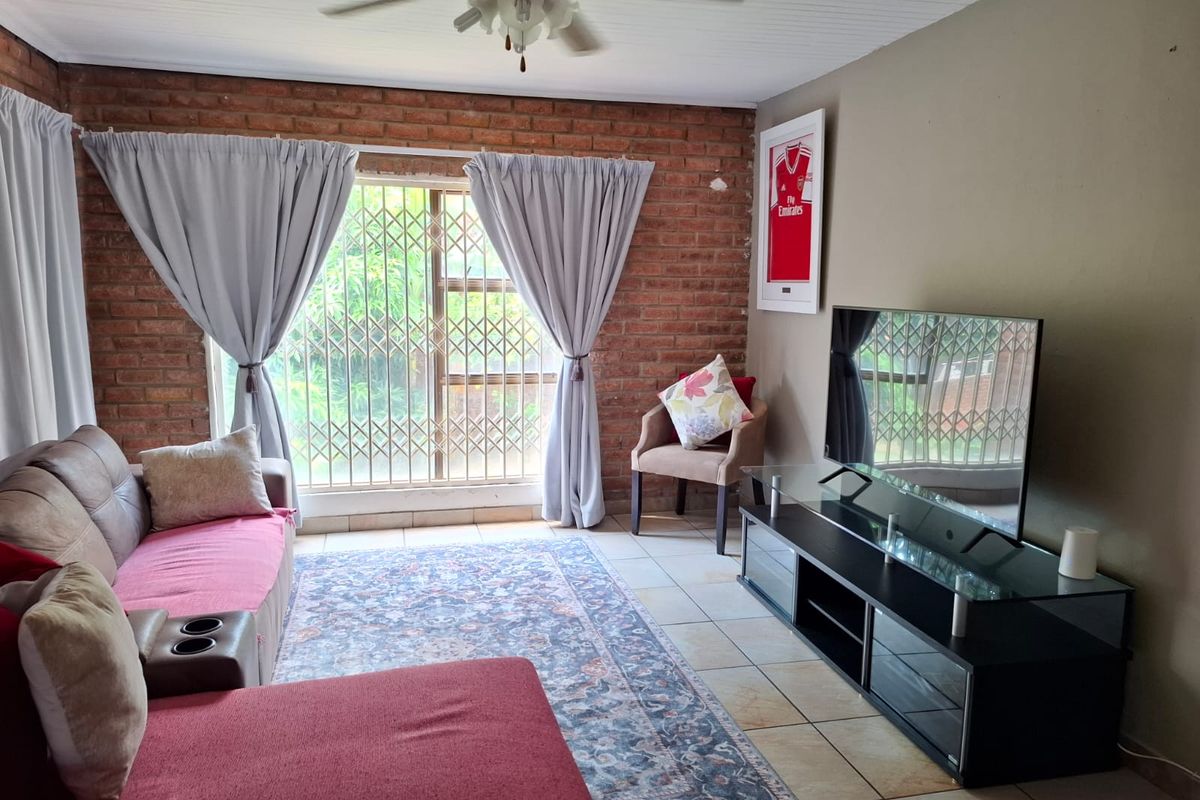 A living room featuring an exposed brick feature wall, tiled flooring, and a ceiling fan, providing a comfortable and functional living space.