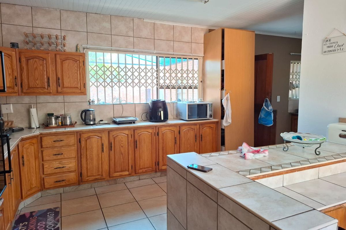 A functional kitchen featuring wooden cabinetry, tiled countertops, and a tiled backsplash, with a breakfast bar area and security bars on the window.