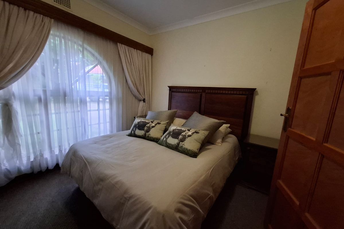 A cozy bedroom featuring a large arched window with wooden trim, neutral carpeting, and a classic wooden door.