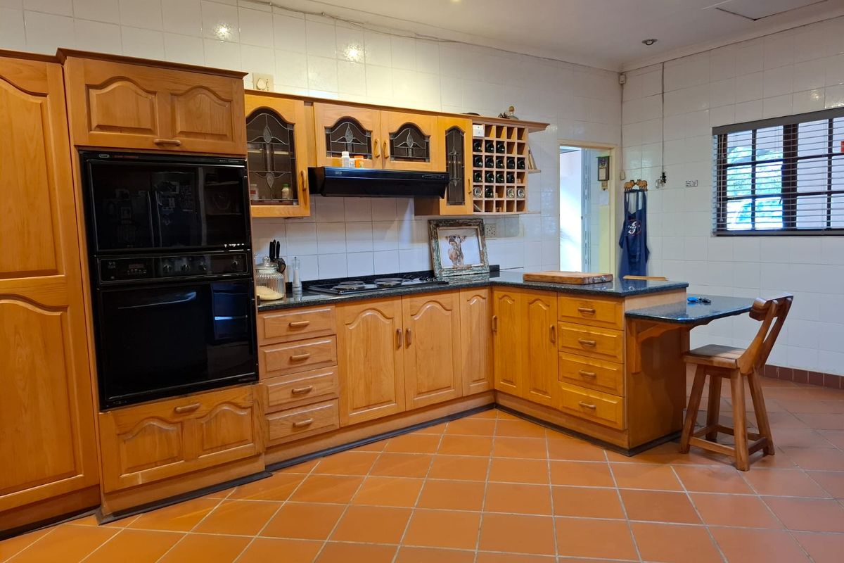 A traditional kitchen featuring timber cabinetry, integrated oven, hob, extractor fan, and a breakfast bar with terracotta floor tiles.