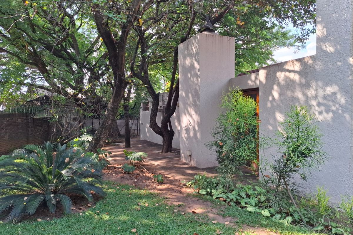 A private rear garden area featuring mature trees, established landscaping, and a paved patio space adjacent to the building's exterior wall.