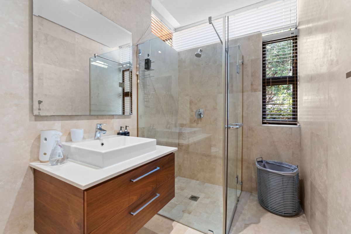 Modern bathroom featuring a floating wood vanity, stone-tiled walls, a glass-enclosed walk-in shower, and clerestory windows for natural light.