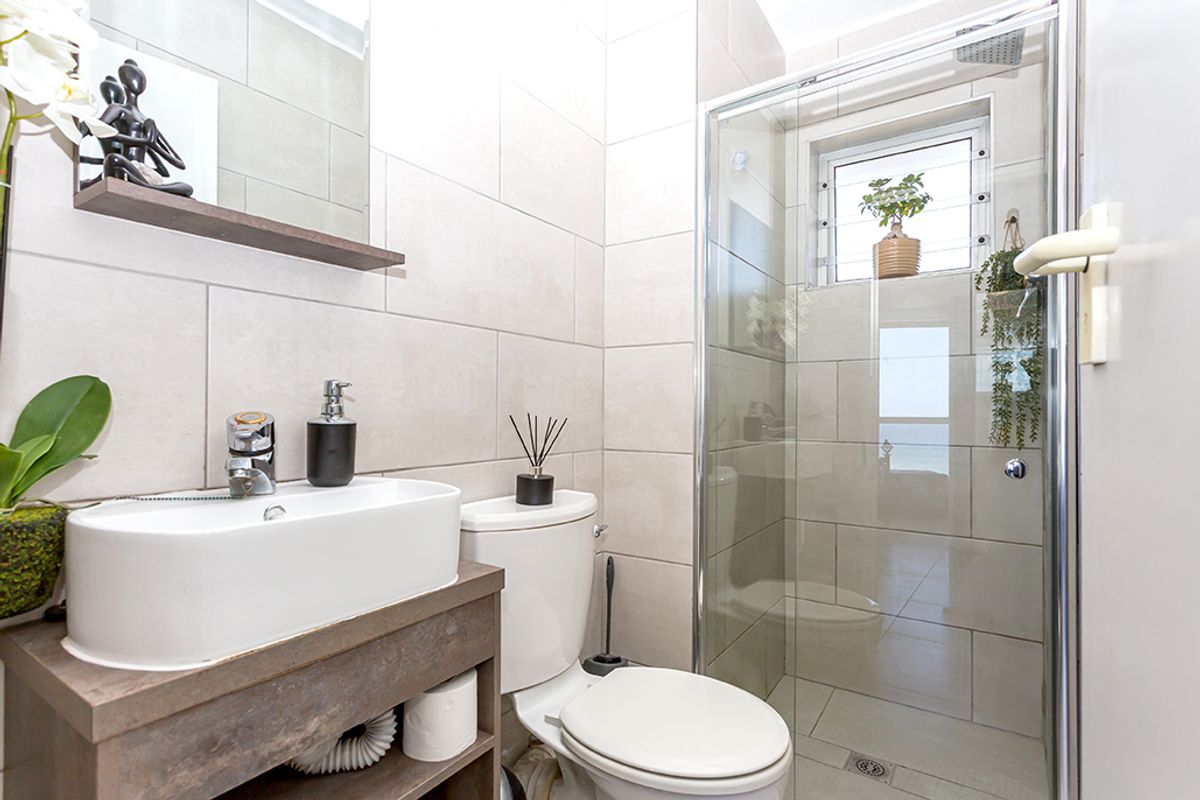 Modern bathroom featuring a vessel sink on a vanity cabinet, a toilet, and a glass-enclosed shower with neutral wall and floor tiling.