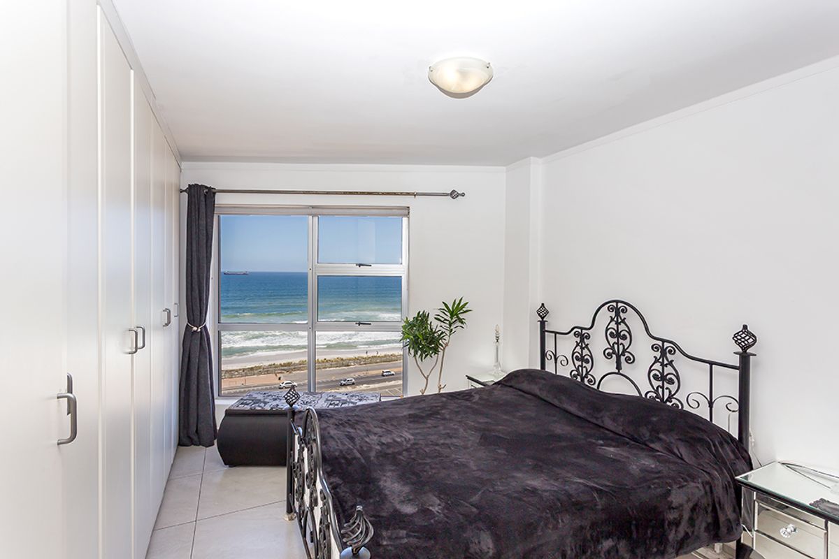 A bright bedroom featuring built-in cupboards, tiled flooring, and a large window offering expansive ocean views.