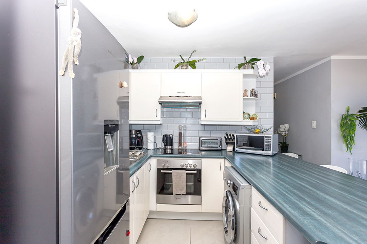 Compact kitchen featuring white cabinetry, subway tile backsplash, laminate countertops, and built-in appliances including an oven and extractor fan.