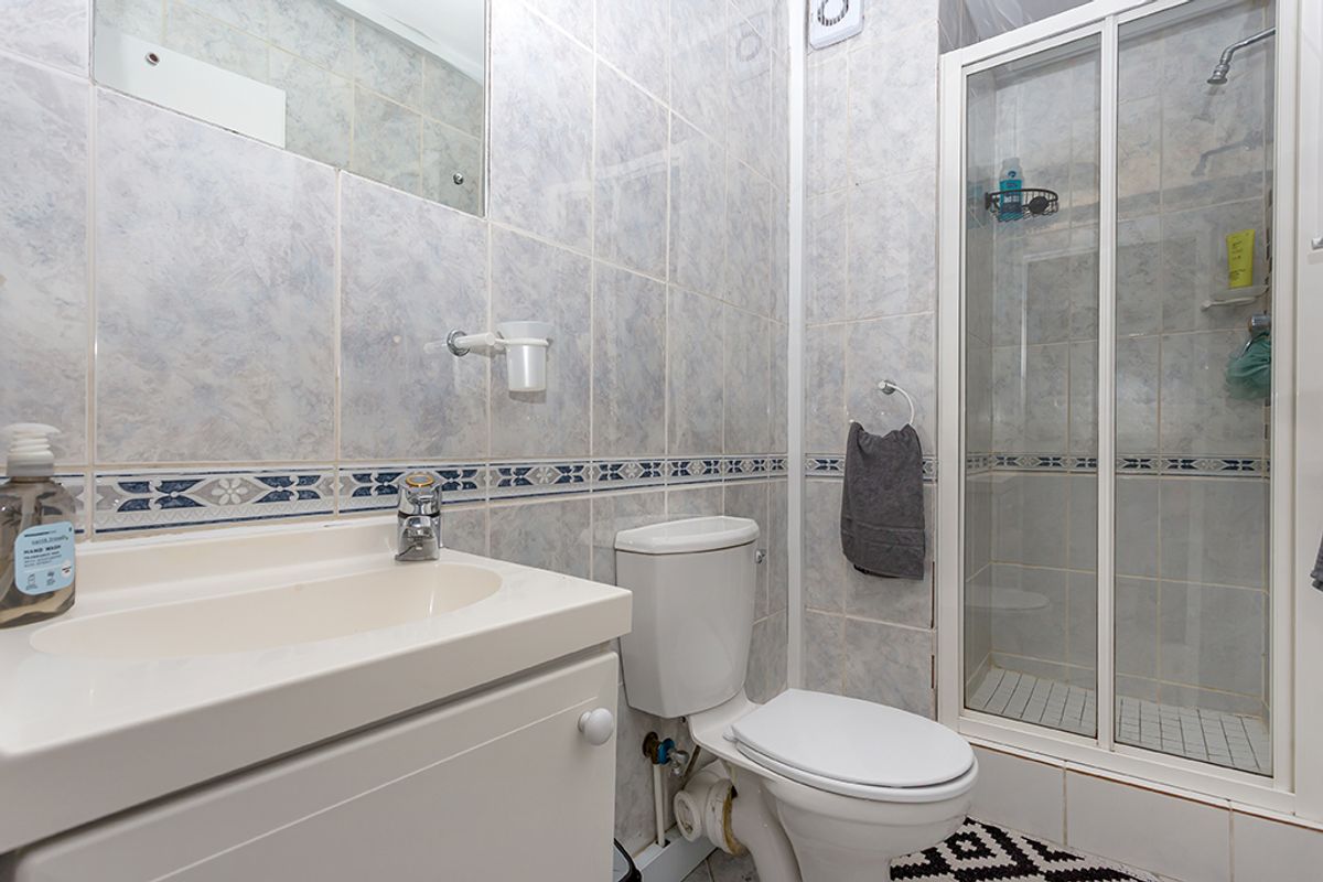 A functional bathroom featuring a shower enclosure, a vanity basin with storage, and a standard toilet, finished with decorative wall tiling.