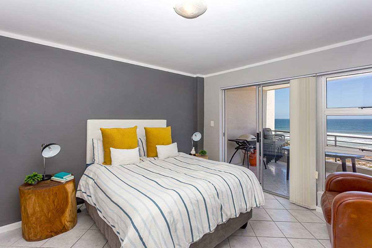 A bright bedroom featuring tiled flooring and sliding glass doors that open onto a balcony with scenic ocean views.