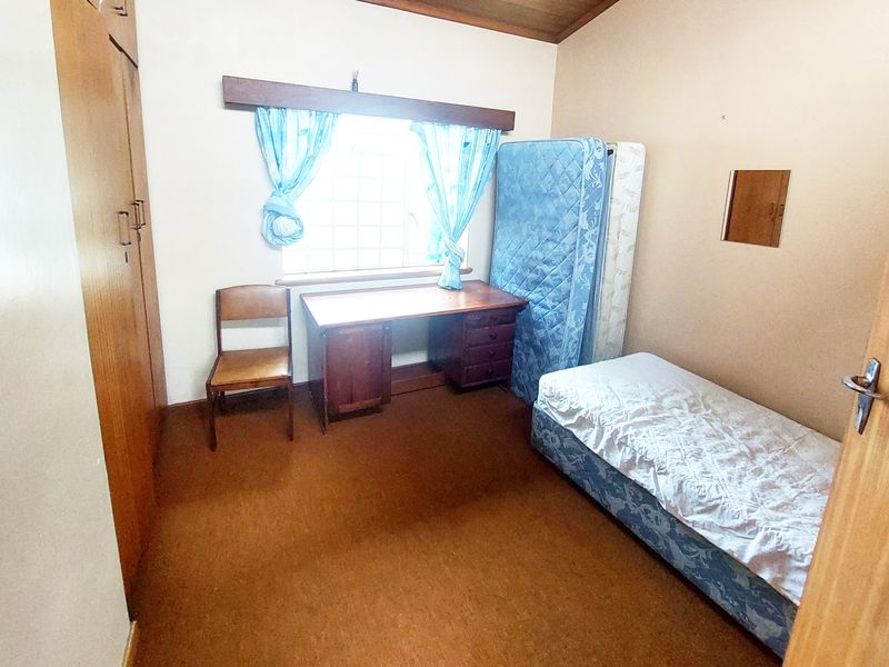 A bedroom featuring built-in cupboards, timber ceiling details, and carpet flooring, offering a functional space in need of cosmetic updates.