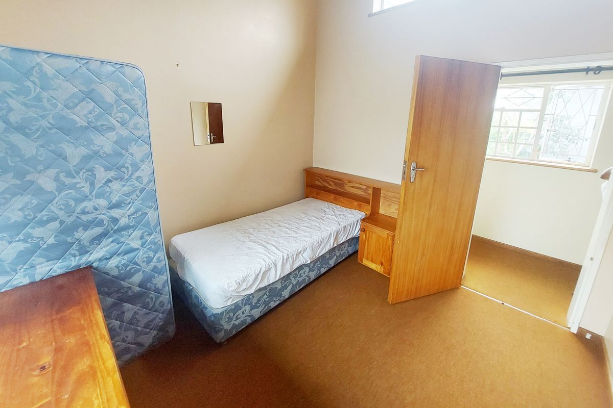 A bedroom featuring carpeted flooring, a built-in headboard, and a window fitted with security burglar bars.