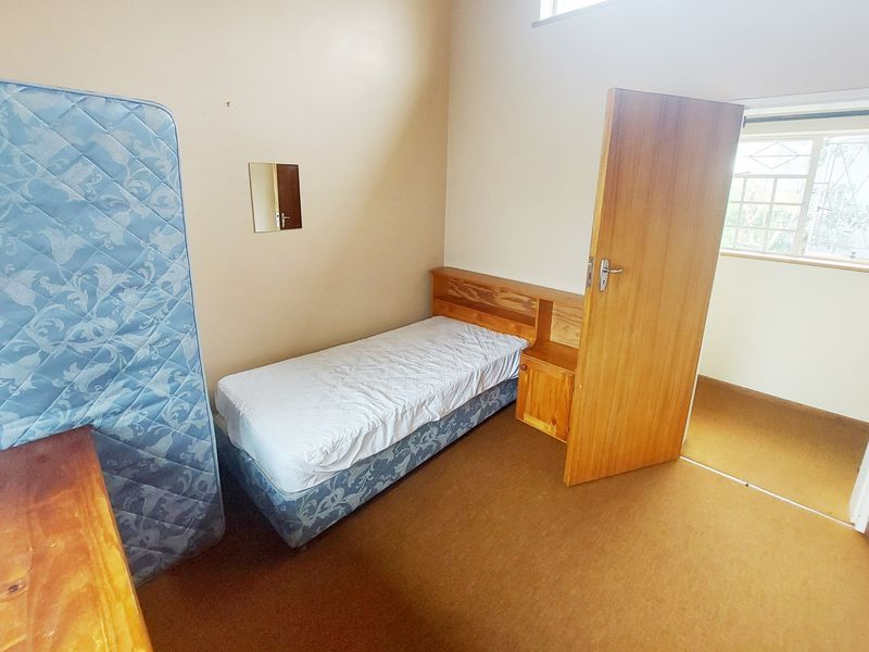 A bedroom featuring carpeted flooring, a built-in headboard, and a window fitted with security burglar bars.