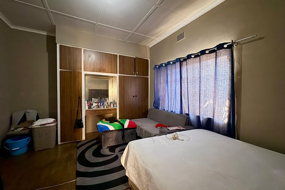 A bedroom featuring built-in wooden cupboards with an integrated vanity area, large window with curtains, and tiled flooring.
