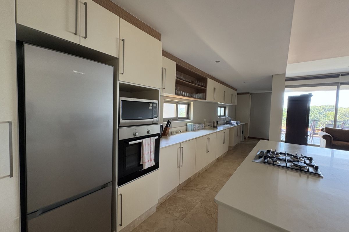 Modern open-plan kitchen featuring stone countertops, built-in oven, gas hob on the island, and ample cabinetry with integrated appliance space.