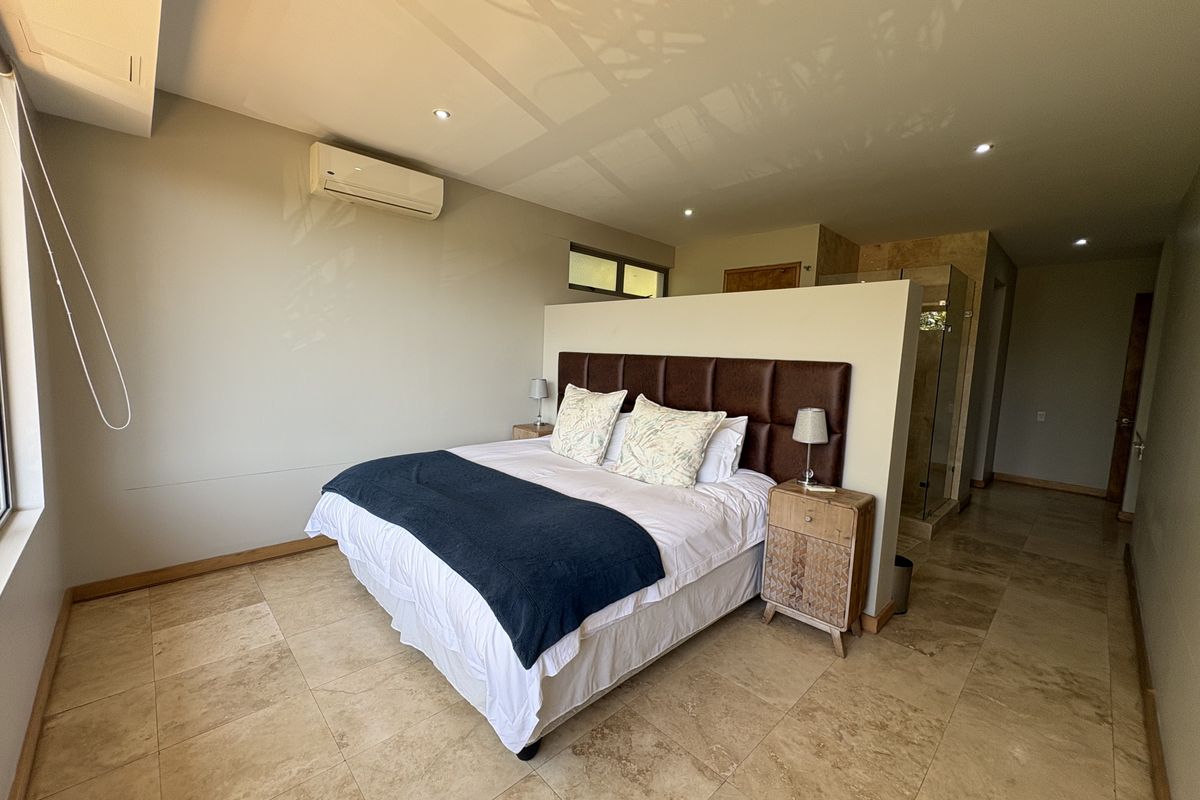 Spacious bedroom featuring travertine flooring, recessed lighting, a split-system air conditioner, and an open-plan layout with an integrated glass-enclosed shower area.