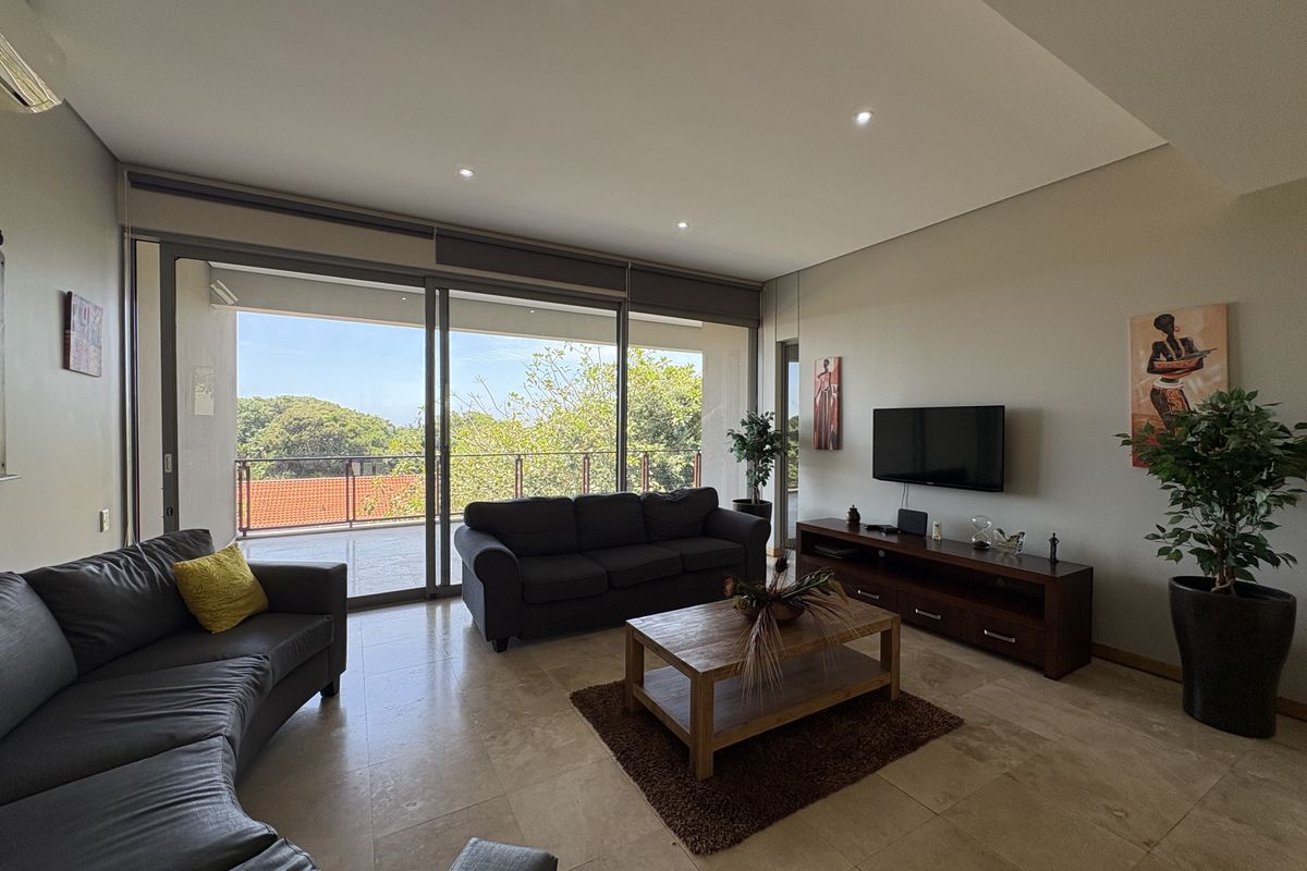Spacious living room featuring travertine flooring, recessed lighting, and large sliding glass doors opening onto a balcony with scenic views.