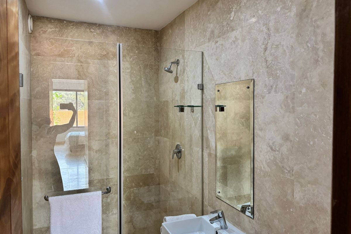 Modern bathroom featuring floor-to-ceiling travertine tiling, a glass-enclosed shower, and a contemporary vessel sink with chrome fixtures.