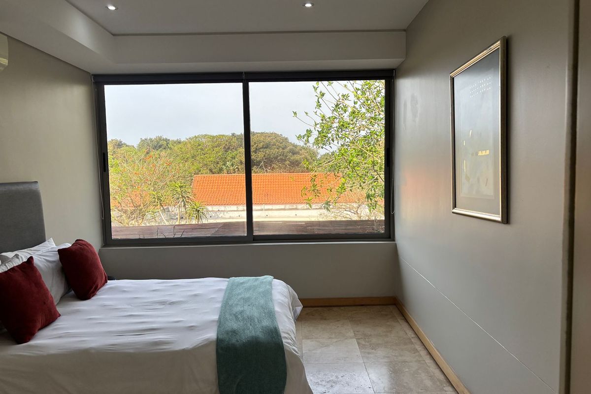 A well-maintained bedroom featuring stone tile flooring, recessed ceiling lighting, and a large sliding window offering a pleasant outdoor view.