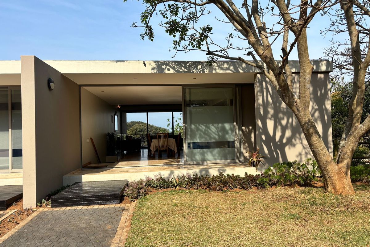 Rear view of a modern townhouse featuring a paved walkway, concrete patio, and large sliding glass doors leading into the open-plan living area.