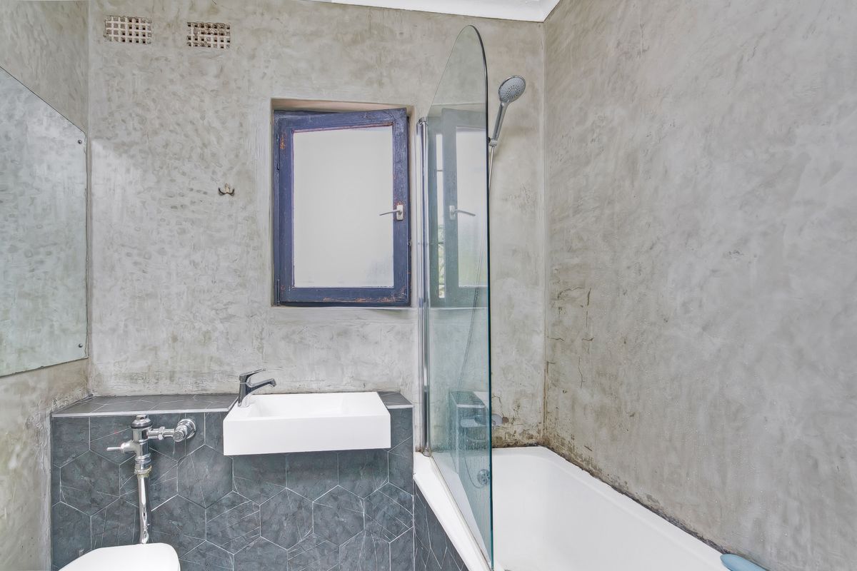 Bathroom featuring a shower-over-bath combination, cement-plastered walls, hexagonal tile backsplash, and a wall-mounted basin.