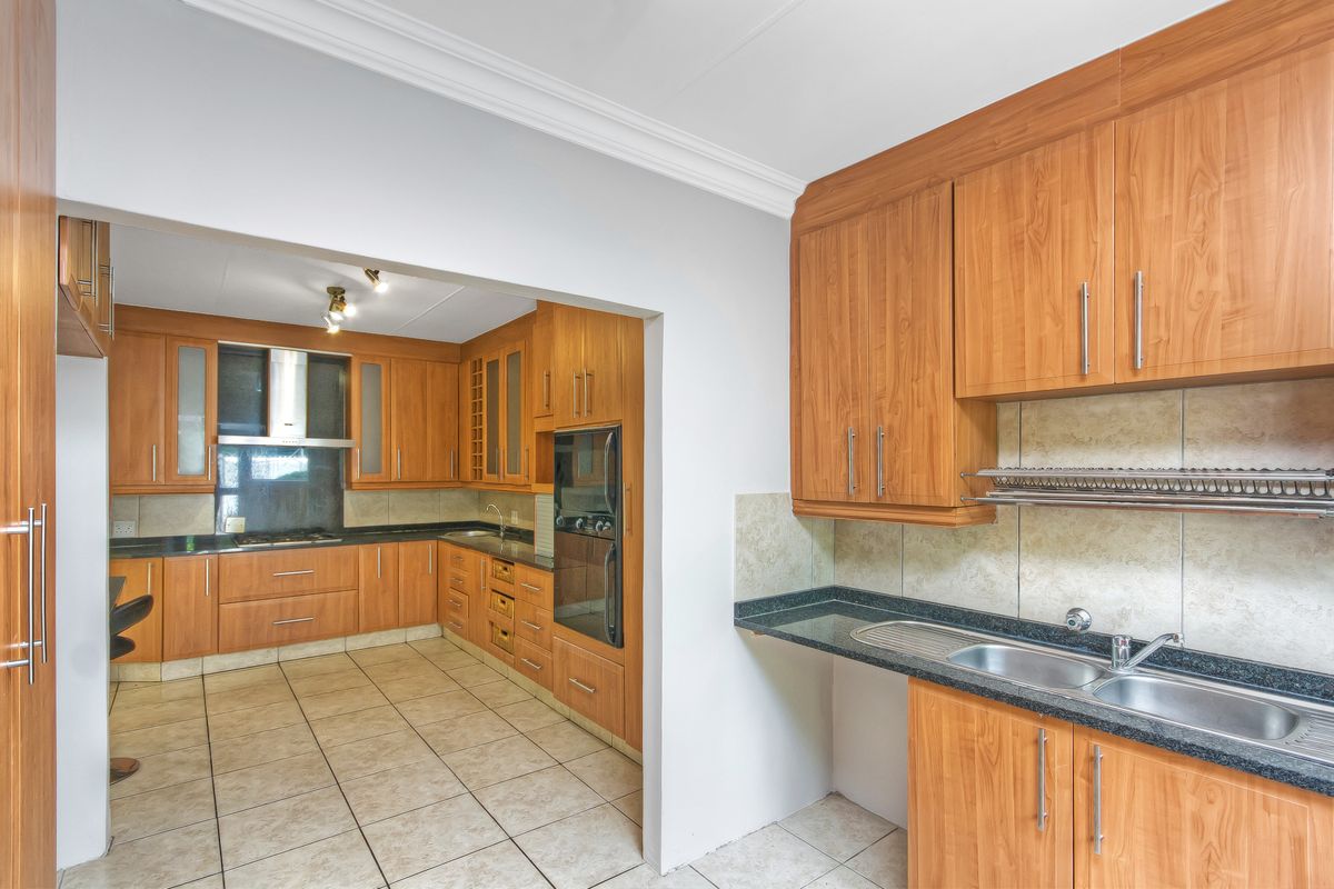 Spacious kitchen featuring wood-veneer cabinetry, granite countertops, a built-in oven, and a separate scullery area with a double sink.