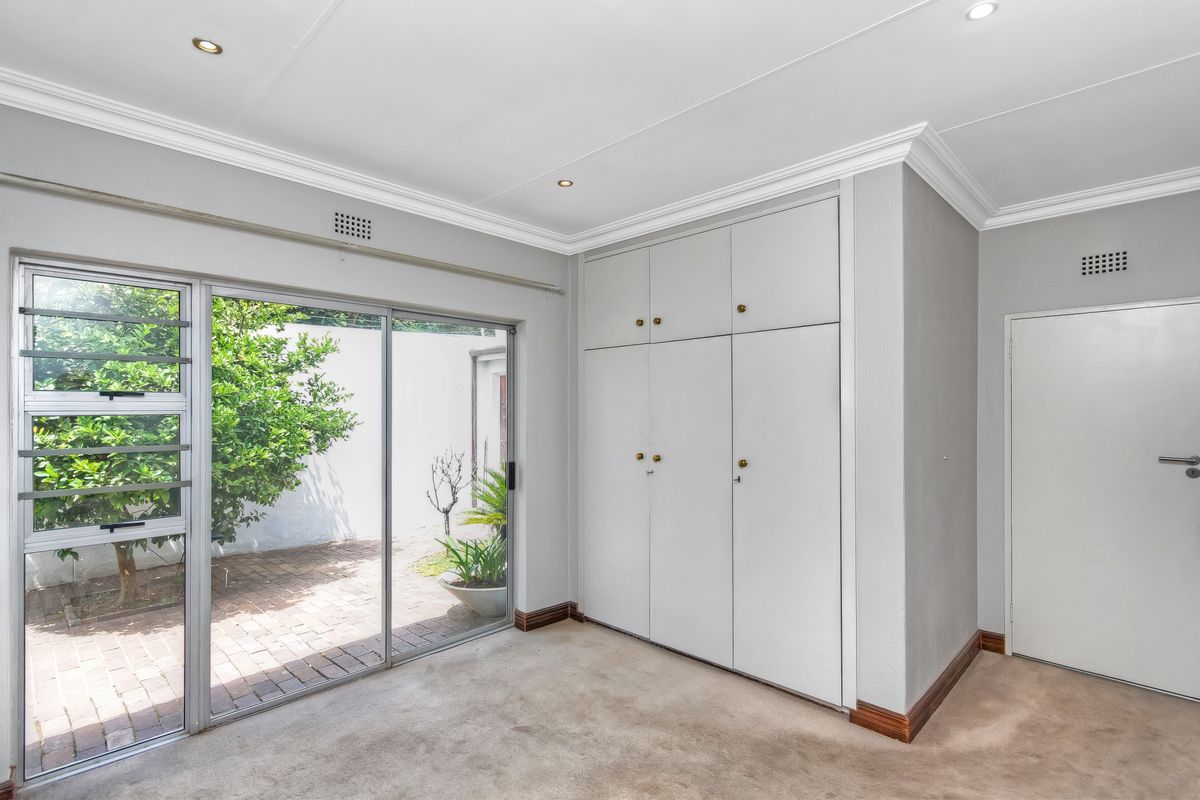 A bright bedroom featuring built-in cupboards, carpeted flooring, and sliding glass doors providing direct access to a private paved courtyard.