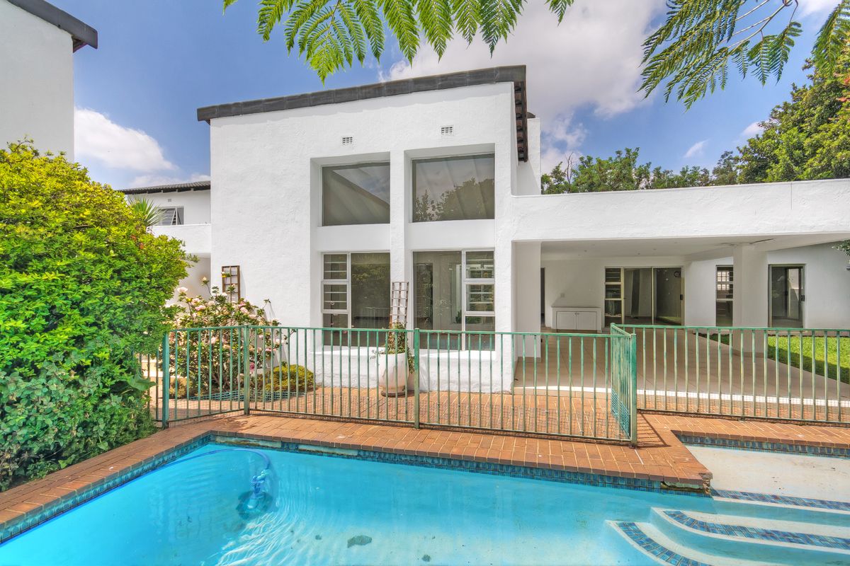 Rear view of the property featuring a swimming pool, paved pool deck, metal safety fencing, and a covered patio area.