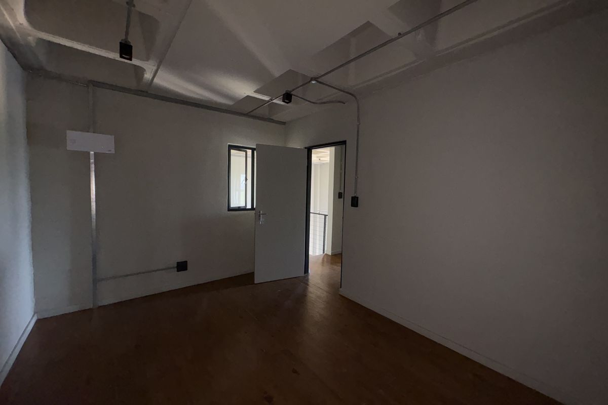 An empty, industrial-style room featuring exposed electrical conduit, concrete ceiling, and timber flooring, offering a blank canvas for renovation.