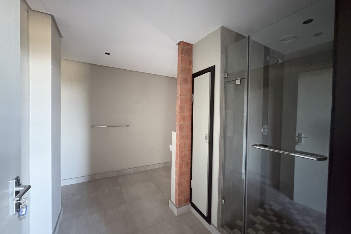 A modern bathroom featuring a glass-enclosed shower, tiled flooring, and a distinctive exposed brick pillar detail.