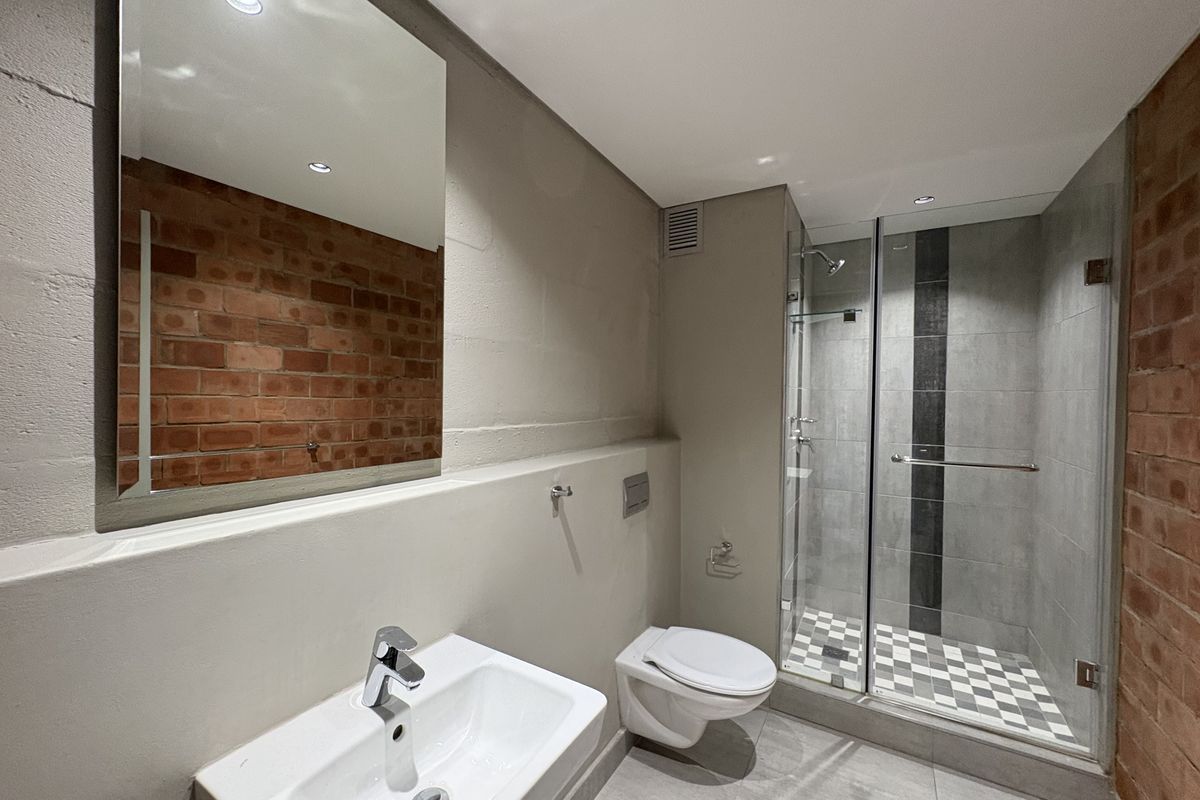 Modern bathroom featuring a glass-enclosed shower, wall-mounted toilet, vanity basin, and exposed brick feature wall.