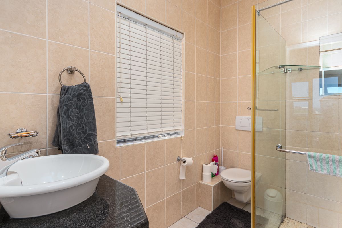 A functional bathroom featuring a vessel sink on a granite vanity, a wall-mounted toilet, and a glass-enclosed shower with neutral wall tiling.