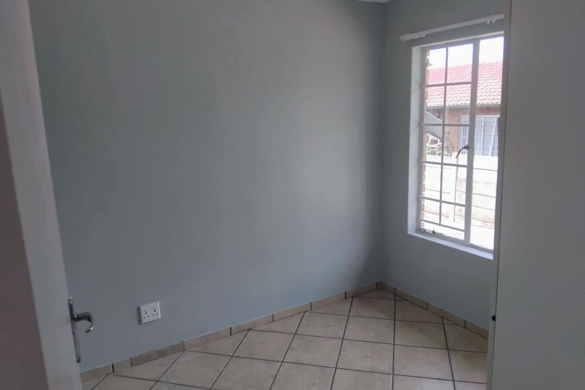 A clean, empty bedroom featuring neutral grey walls, tiled flooring, and a window with security bars, providing a blank canvas for personalization.