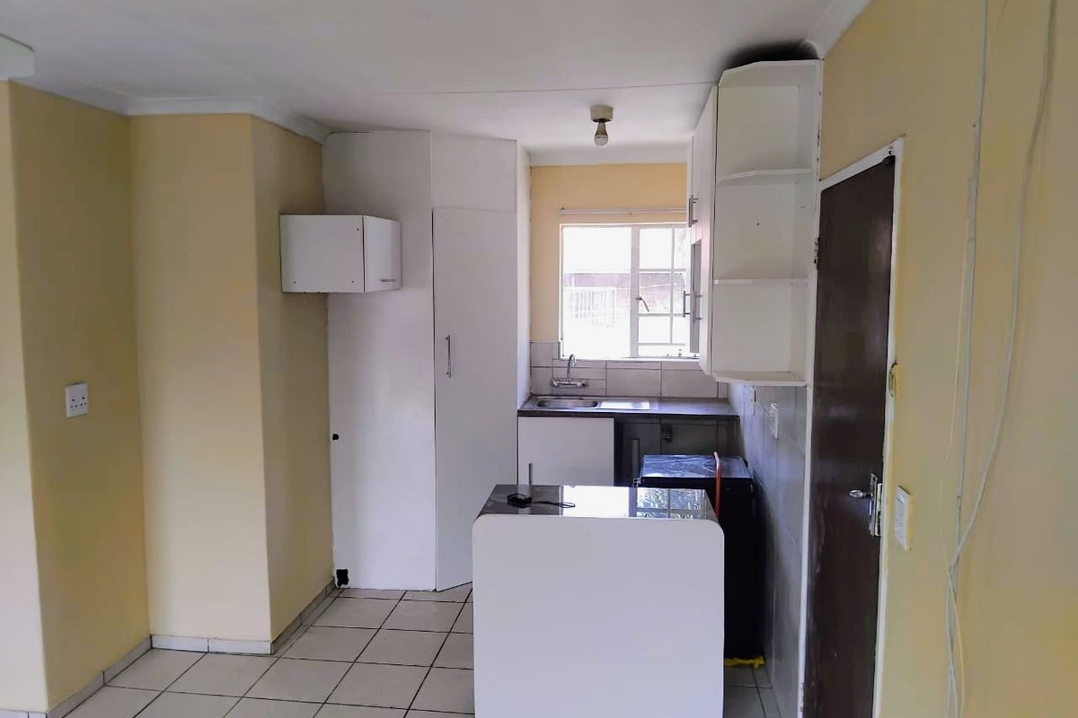 A compact kitchen featuring built-in cabinetry, a stainless steel sink, and tiled flooring, offering a functional space ready for modernization.