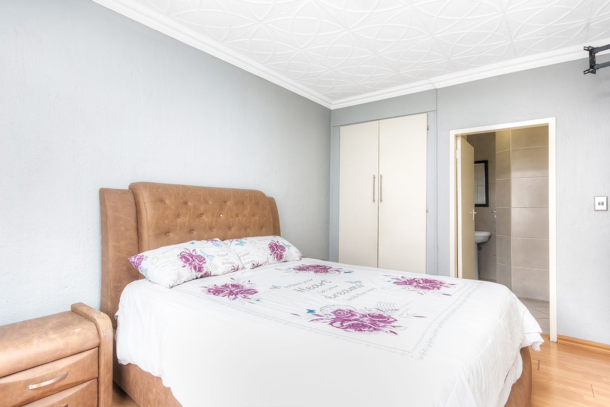 A bedroom featuring laminate flooring, a textured ceiling with coving, and a built-in wardrobe, with direct access to an en-suite bathroom.