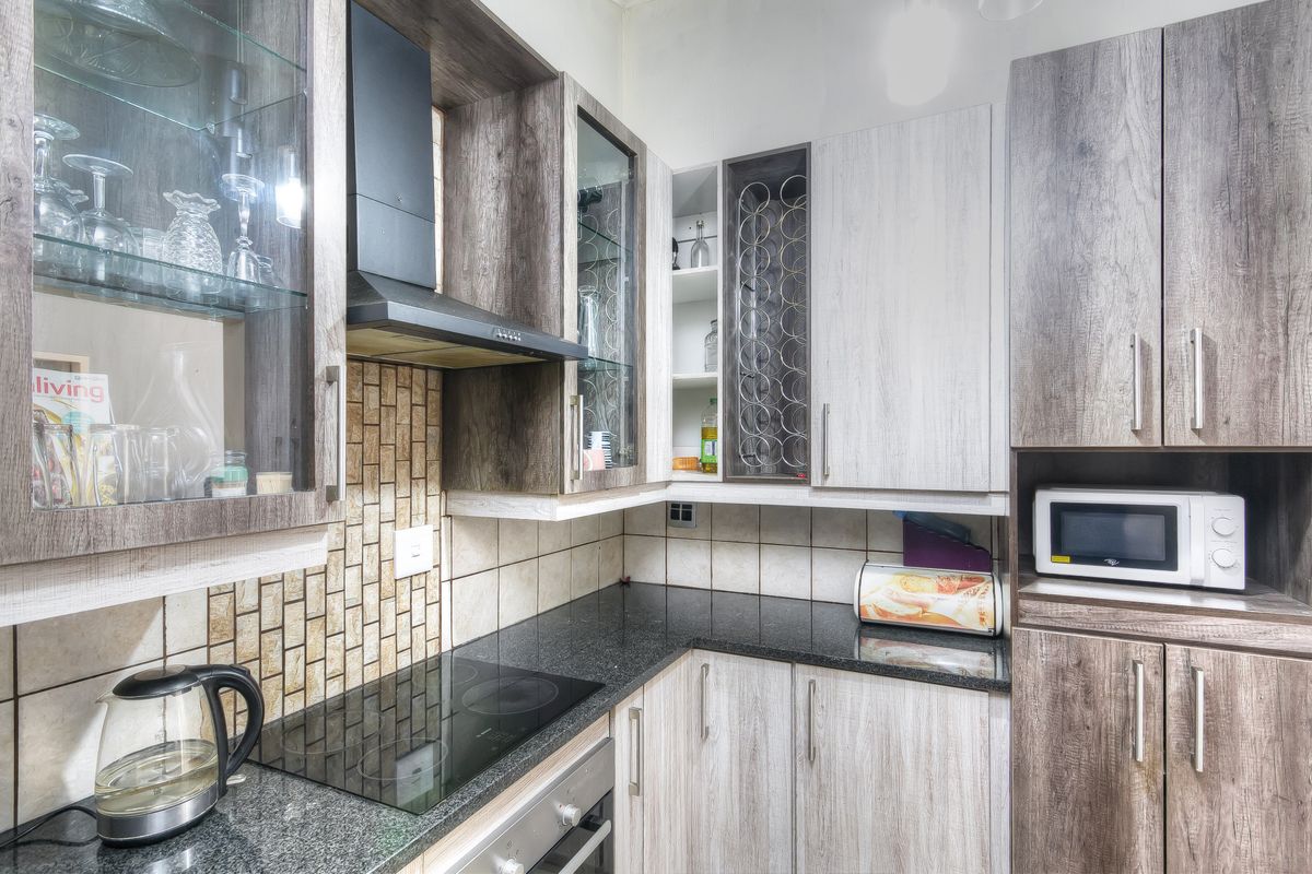 Modern kitchen featuring wood-grain cabinetry, granite countertops, a built-in electric hob, oven, and extractor fan with a decorative tiled backsplash.