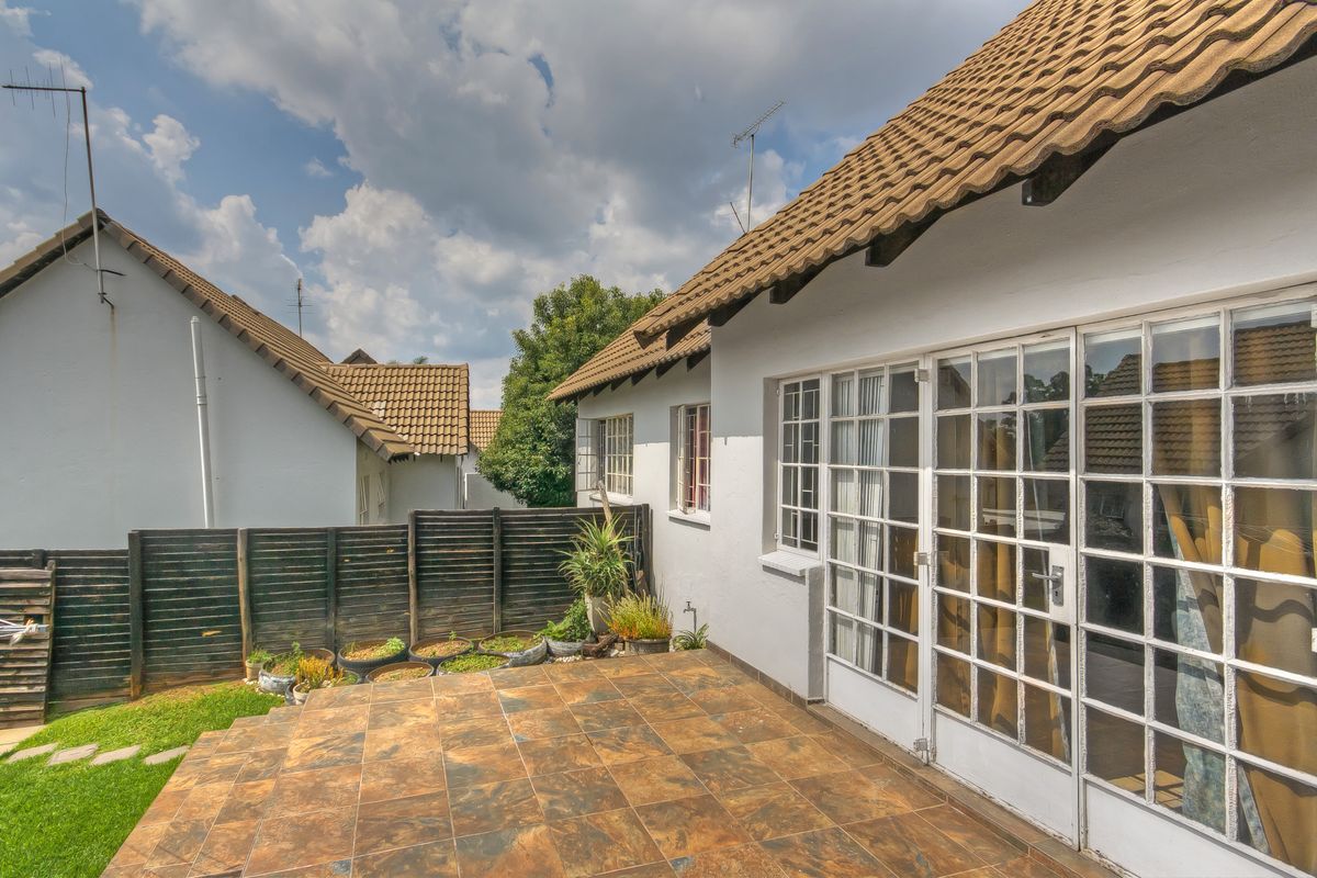 Rear exterior view of the townhouse featuring a tiled patio, white facade, and classic french doors leading into the living space.