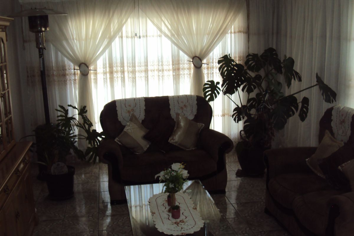 A living room featuring tiled flooring and a large window with sheer curtains, providing natural light to the space.
