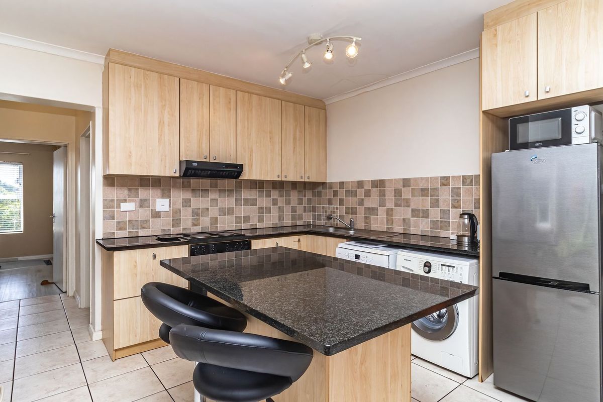 Functional kitchen featuring light wood cabinetry, dark granite countertops, tiled backsplash, and a convenient breakfast nook with integrated appliance space.
