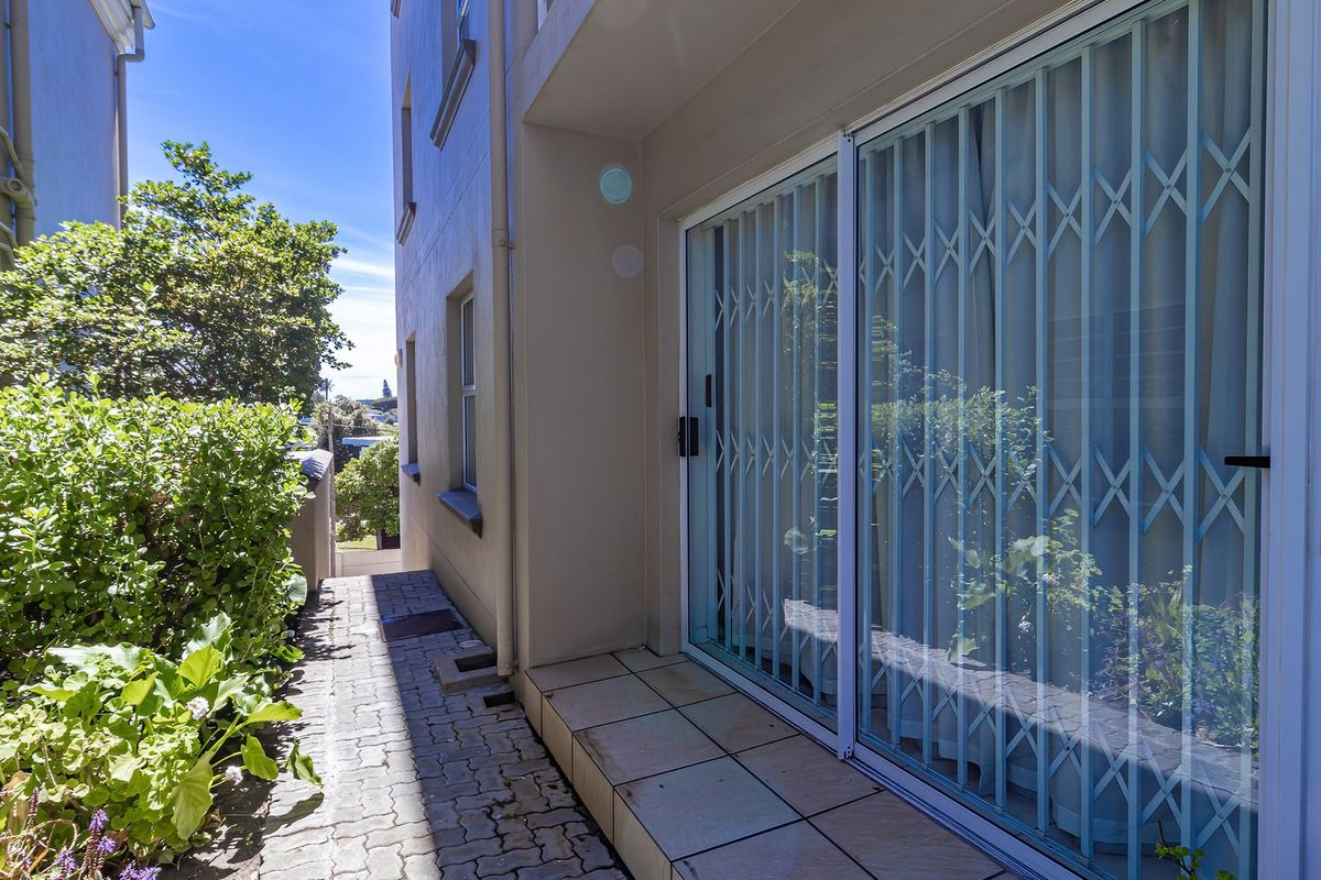 A paved rear exterior walkway featuring a tiled patio area and a sliding glass door with a security gate.