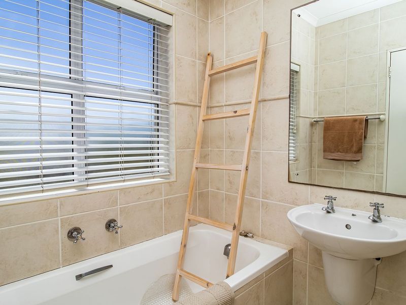 A functional bathroom featuring a built-in bathtub, pedestal basin, wall-mounted mirror, and neutral tiled finishes throughout.