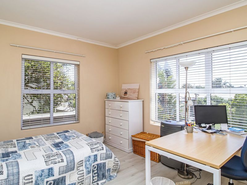 A functional bedroom featuring dual-aspect windows with venetian blinds, neutral wall tones, and durable laminate flooring.
