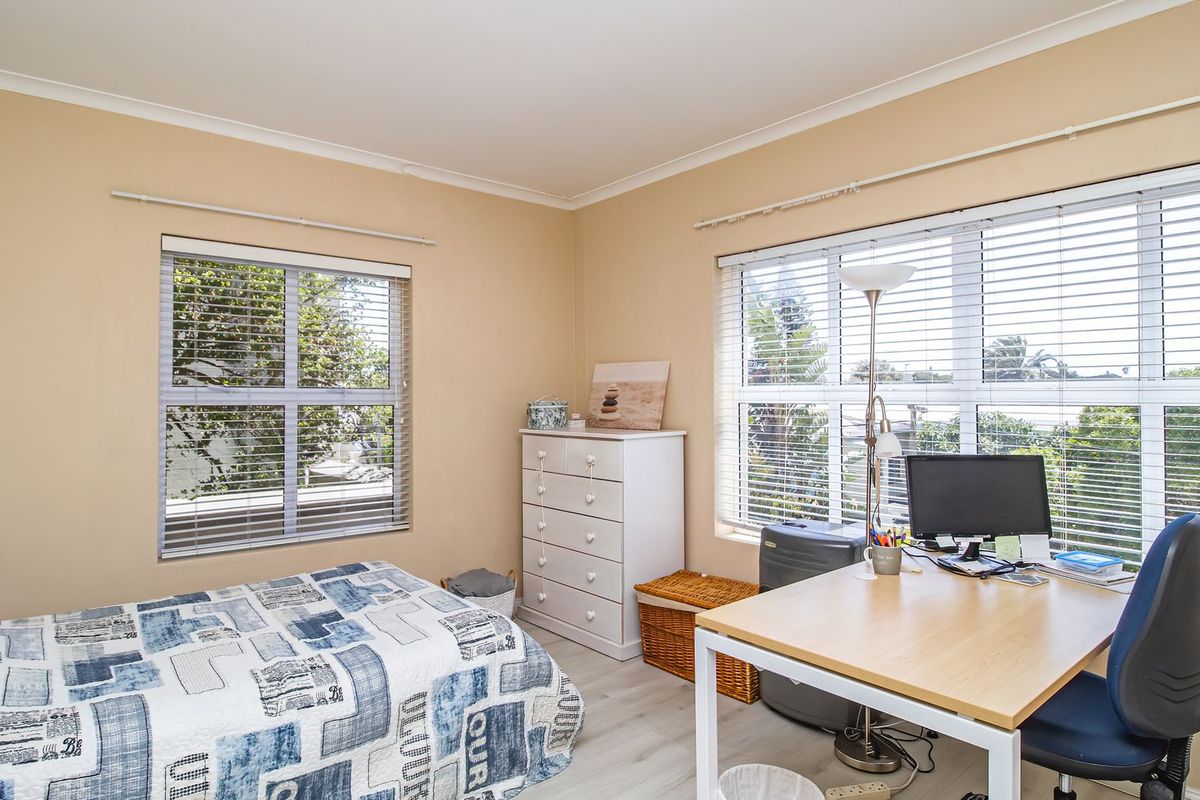 A functional bedroom featuring dual-aspect windows with venetian blinds, neutral wall tones, and durable laminate flooring.